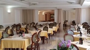 Un salón de banquetes con varias mesas redondas, cada una cubierta con un mantel amarillo y rodeada de sillas de madera.