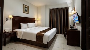 A hotel room with a large bed, bedside lamps, a television, and a desk with a phone and a coffee maker. - Antares Medan (Medan)