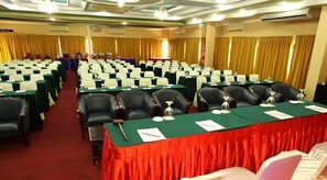 A conference room with rows of chairs, a long table with a red tablecloth, and a stage with a podium. - Antares Medan (Medan)
