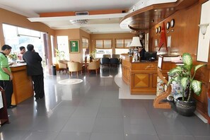 A hotel lobby with a reception desk, seating area, and a large potted plant. - Antares Medan (Medan)