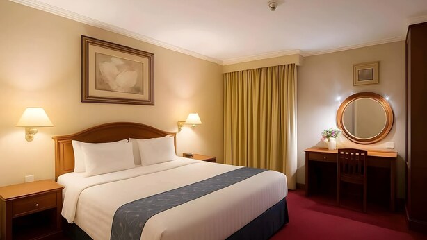 A hotel room with a large bed, two bedside tables, a desk with a chair, a mirror, and a window with curtains. - Antares Medan (Medan)