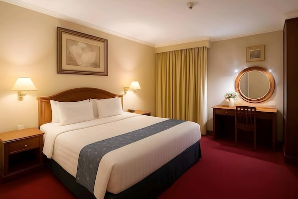 A hotel room with a large bed, two bedside tables, a desk with a chair, a mirror, and a window with curtains. - Antares Medan (Medan)
