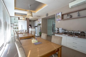 Un comedor moderno con una larga mesa de madera, varias sillas y una cocina al fondo.