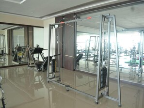 Un gimnasio con equipo de ejercicio, un espejo grande y vistas a otras instalaciones deportivas.