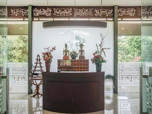 Un mostrador de recepción con un cartel que dice 'Bali Kedaton Resort', rodeado de plantas en macetas y objetos decorativos.