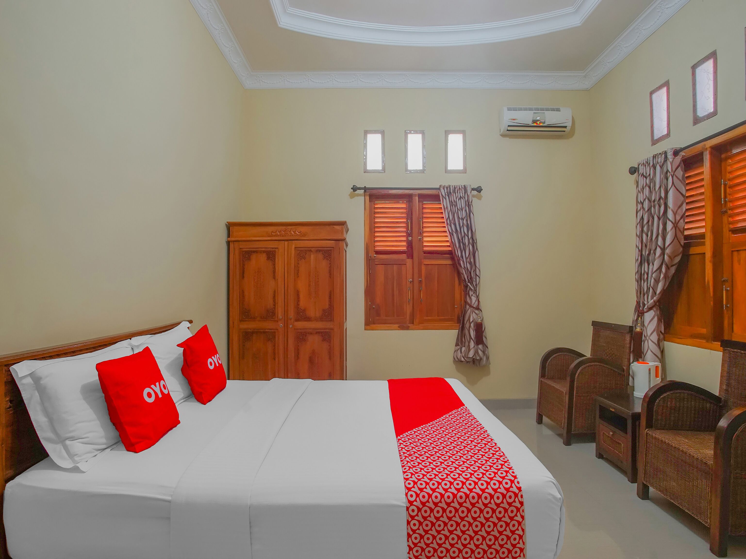 A hotel room with a bed, two chairs, a wardrobe, and a window with shutters.