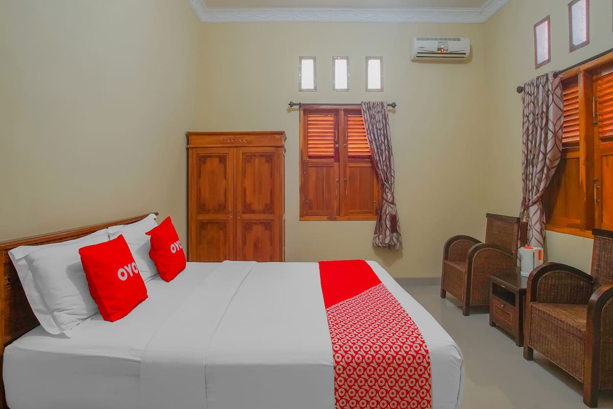 Habitación de hotel con cama, dos sillas, armario y ventana con persianas.