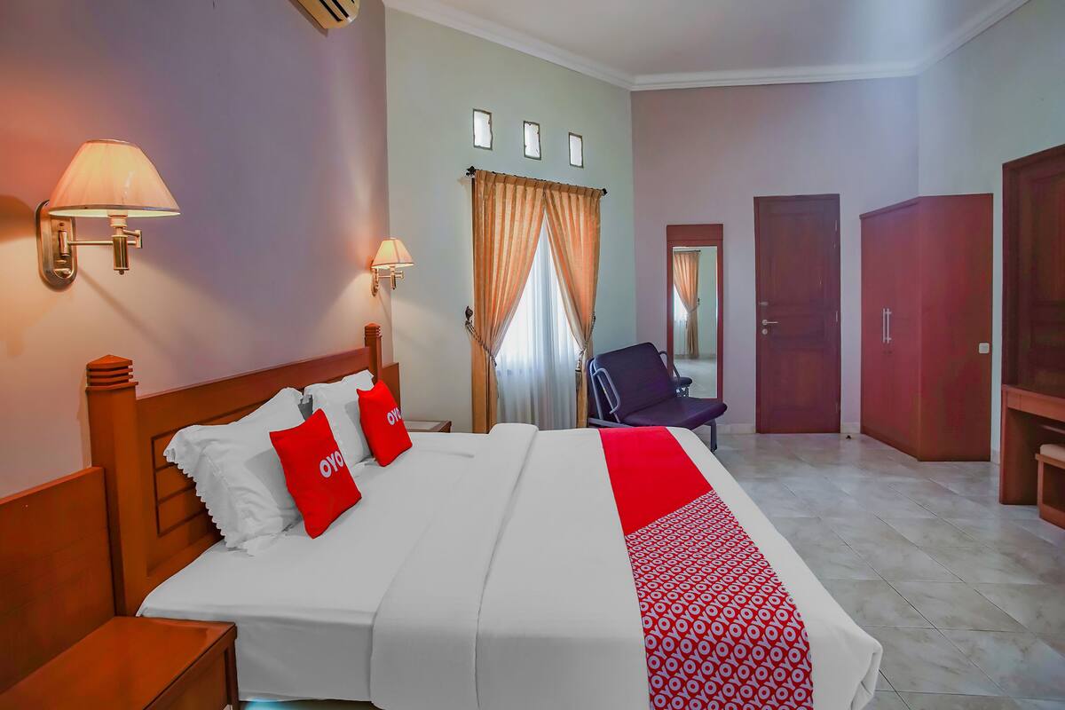 Ein Hotelzimmer mit einem großen Bett, zwei Nachttischlampen, einem Sessel, einem Kleiderschrank und einem Spiegel.