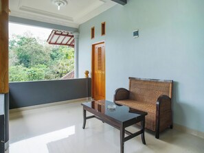 A balcony with a wicker chair and a glass-top table, a wooden door, and a view of greenery. - OYO 89999 Hotel Bumi Kedaton Resort (Bandar Lampung)