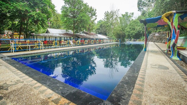 A swimming pool with a reflection of trees and a covered area with colorful railings. - OYO 89999 Hotel Bumi Kedaton Resort (Bandar Lampung)