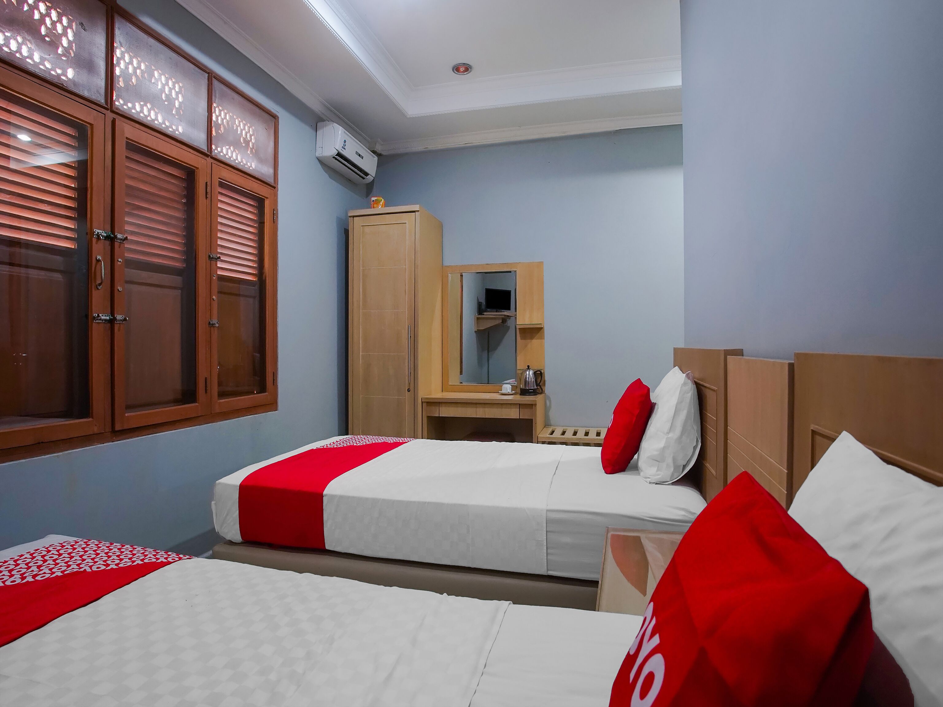 A hotel room with two beds, a wardrobe, a mirror, and an air conditioning unit.