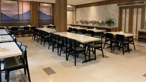 A spacious dining area with long tables and chairs, a marble wall, and a large window with a mountain view. - Bintang Mulia Hotel (Jember)