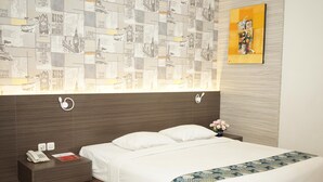 A hotel room with a large bed, white bedding, a nightstand with a phone, a wall with a cityscape wallpaper, and a painting above the bed. - Bintang Mulia Hotel (Jember)