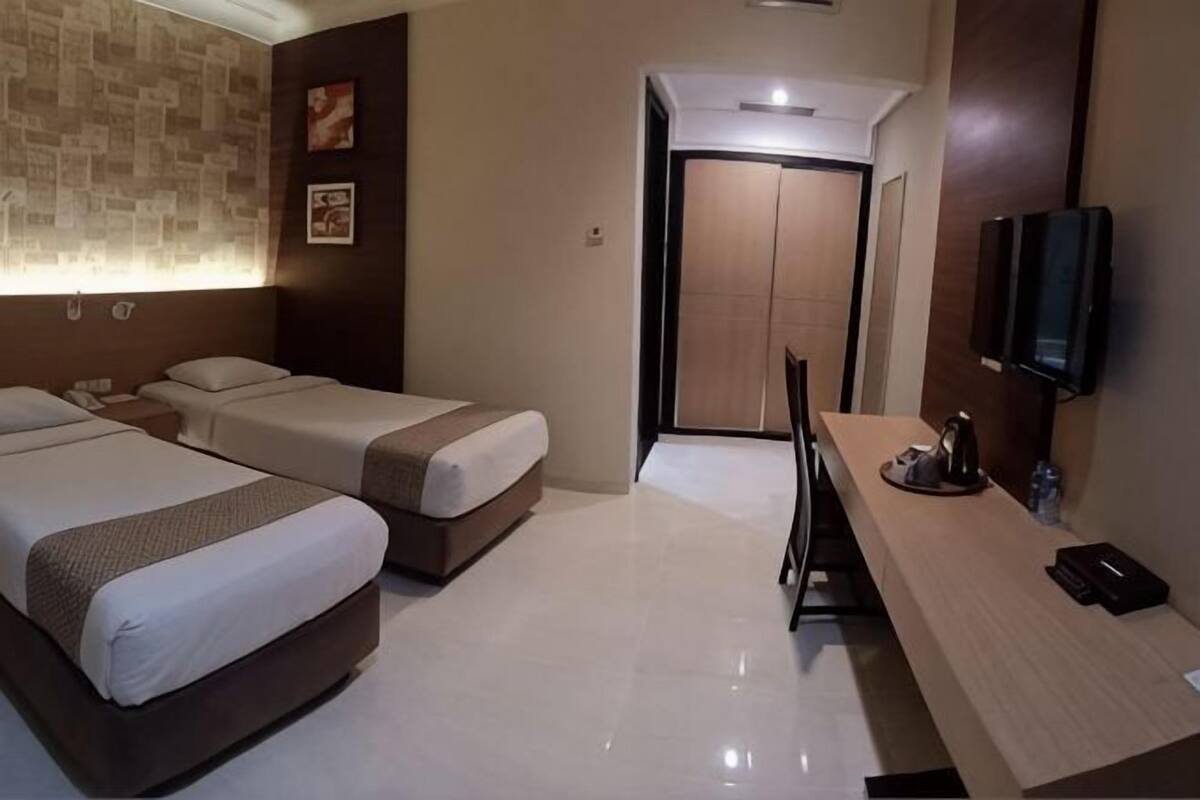 Habitación de hotel con dos camas, un escritorio, una silla, un televisor y una puerta que da a un baño.