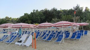 A beach with rows of blue lounge chairs and red and white striped umbrellas. - Hotel Incoronato (Capo Vaticano)