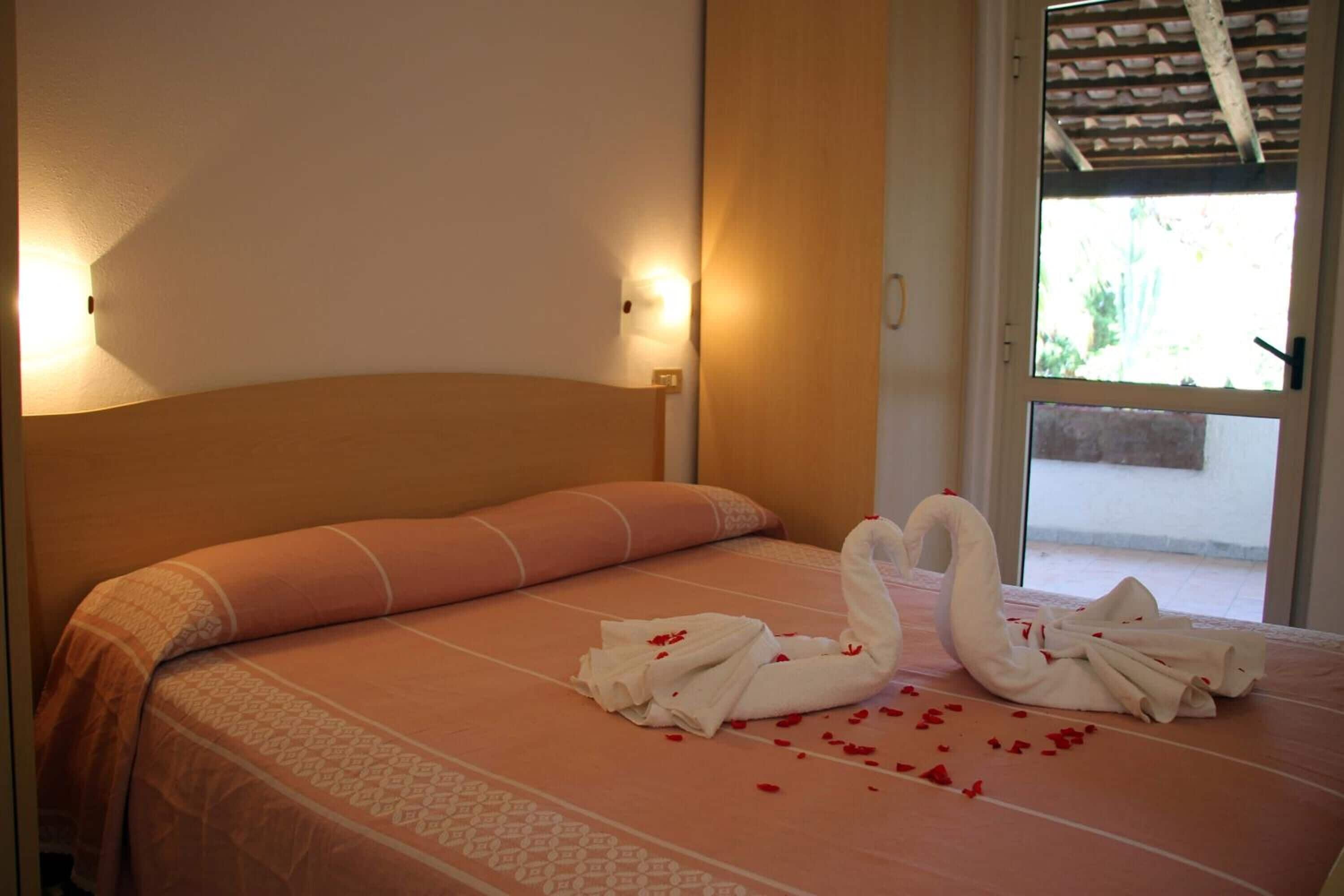 A hotel room with a bed, a wall-mounted light, and a window with a view.
