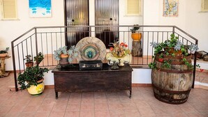 A wooden bench with decorative items and potted plants in a courtyard with a metal railing and doors in the background. - Hotel Incoronato (Capo Vaticano)