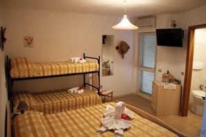 A dormitory room with bunk beds, a desk, a mirror, a television, and a bathroom.