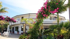 A two-story building with a balcony, surrounded by lush greenery and flowering plants. - Hotel Incoronato (Capo Vaticano)