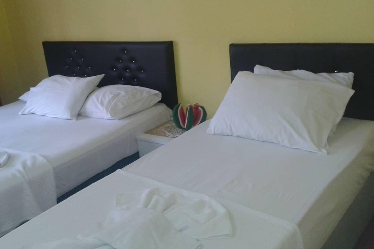 Two single beds with white linens and headboards, a small bedside table with a decorative item, and a plain yellow wall.