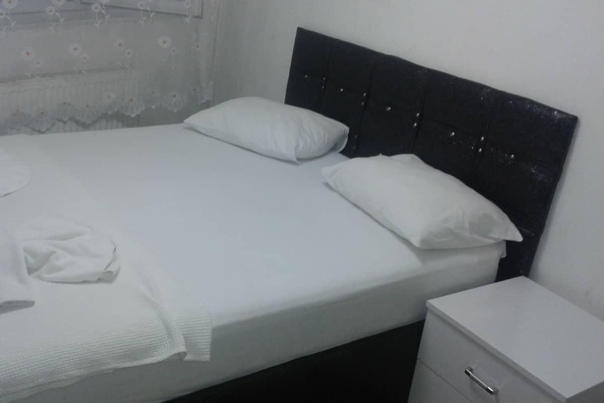 A neatly made bed with white linens, a dark headboard, and a small bedside table with a drawer.