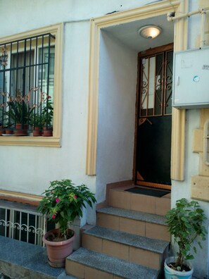 A building entrance with a set of stone steps leading to a door, a window with metal bars and potted plants, and a utility box on the wall. - Bereket Apart Hotel (Istanbul)