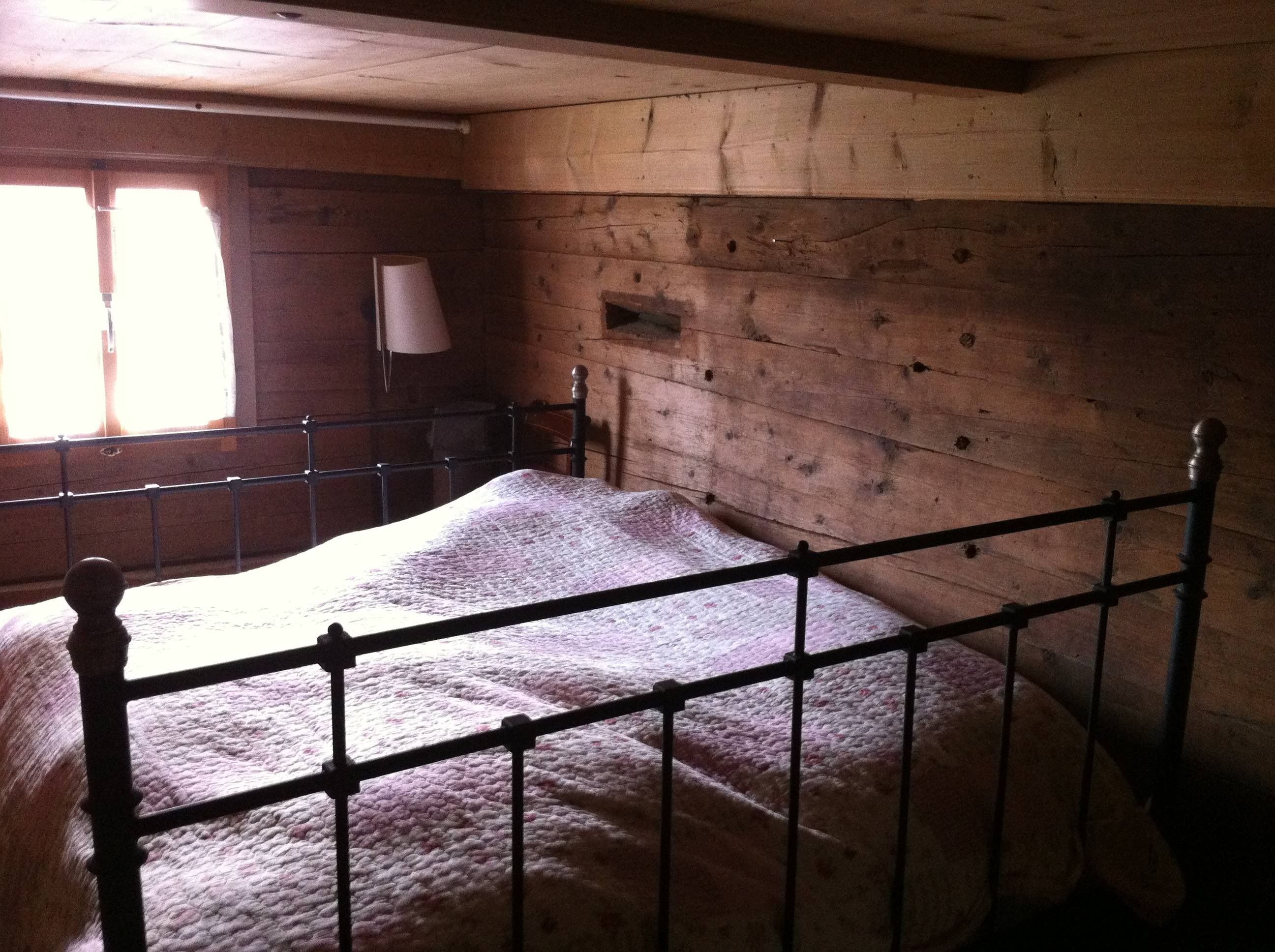 A wooden room with a metal bed frame and a quilted bedspread.