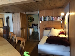 A cozy room with a wooden ceiling, a white sofa with a red blanket, a bookshelf with books, and a wooden chair.
