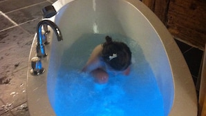 A bathtub with a person inside, a faucet, and a control button. - 400 Year Old Swiss Chalet (Boltigen)