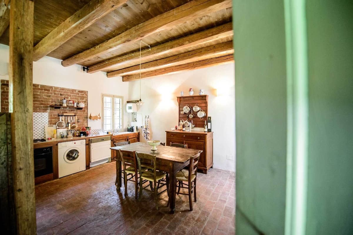 Une cuisine rustique avec des poutres apparentes, un mur en briques et une table à manger en bois, accompagnée de chaises.