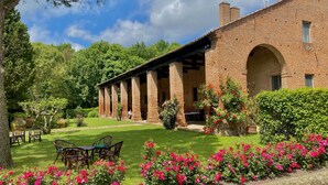 Un bâtiment en briques doté d’un patio couvert, entouré d’une végétation luxuriante et de plantes à fleurs.