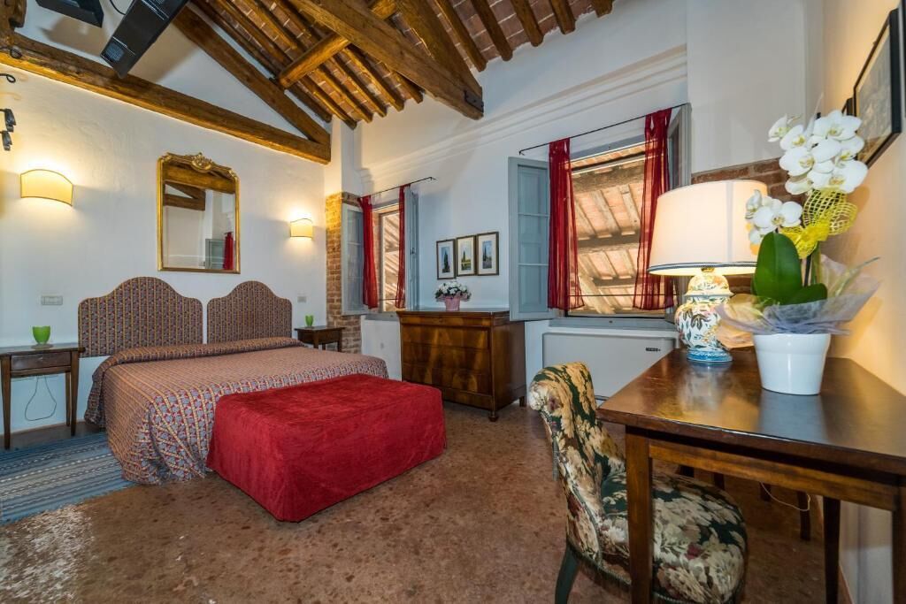 A bedroom with a bed, a desk, a chair, a mirror, and a window with red curtains.