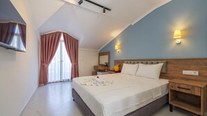 A hotel room with a large bed, a flat-screen TV mounted on the wall, a bedside table with a lamp, and a window with curtains.