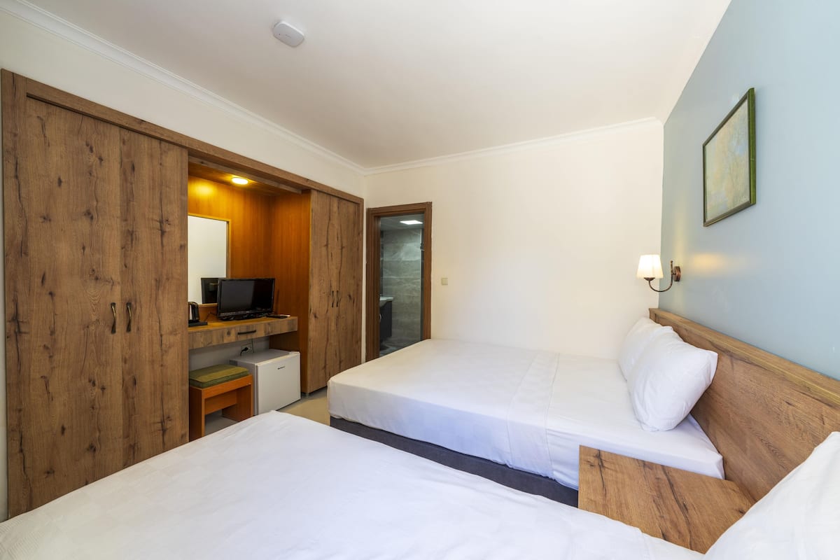 A hotel room with two beds, a wooden wardrobe, a desk with a computer, and a small table.