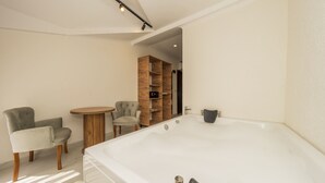 A modern bathroom with a large bathtub, two chairs, a small round table, and a wooden shelving unit.
