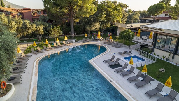 A swimming pool with sun loungers and umbrellas, surrounded by trees and a hotel named "KATRE HOTEL ÖLDENİZ".