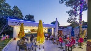 An outdoor seating area with tables and chairs, umbrellas, and a bar area with a sign reading "KATRE Bar".