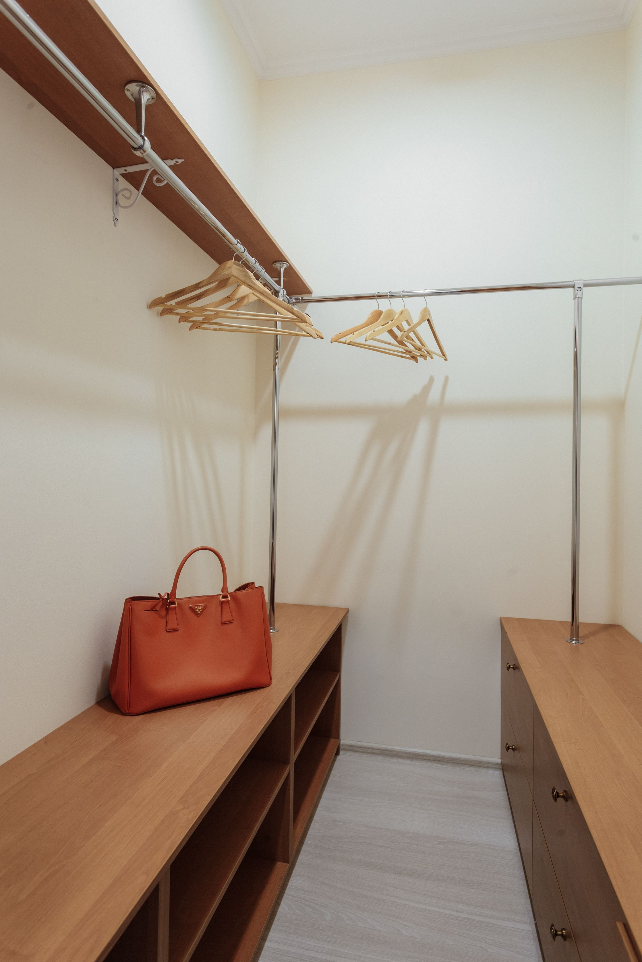 A walk-in closet with wooden shelves, a hanging rack, and a single brown handbag.