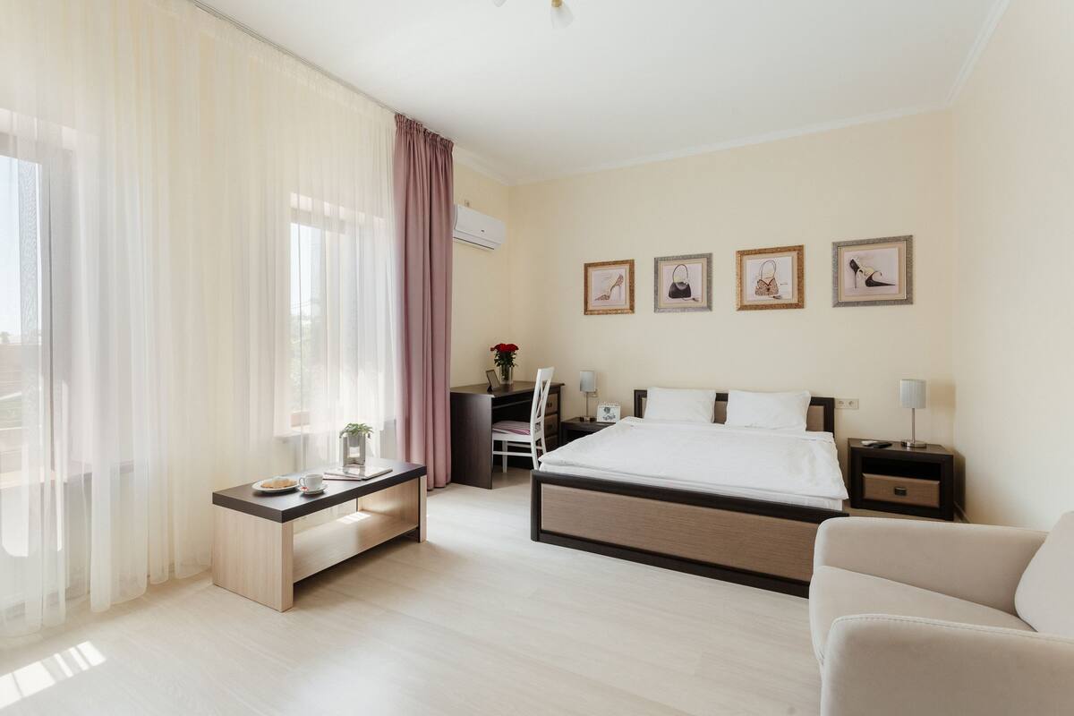 A hotel room with a bed, bedside tables, a desk, a chair, and a sofa.