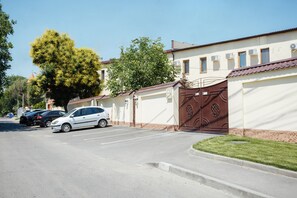 A parking lot with a gated entrance, a white building with multiple windows, and a large tree in the background. - Asiya Hotel (Odesa)