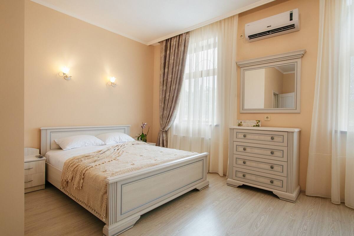 A bedroom with a bed, nightstand, dresser, mirror, and window with curtains.