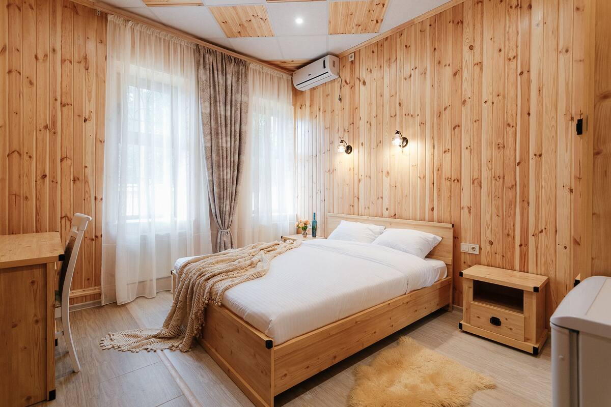 A wooden-paneled bedroom with a bed, bedside tables, a desk, and a chair.