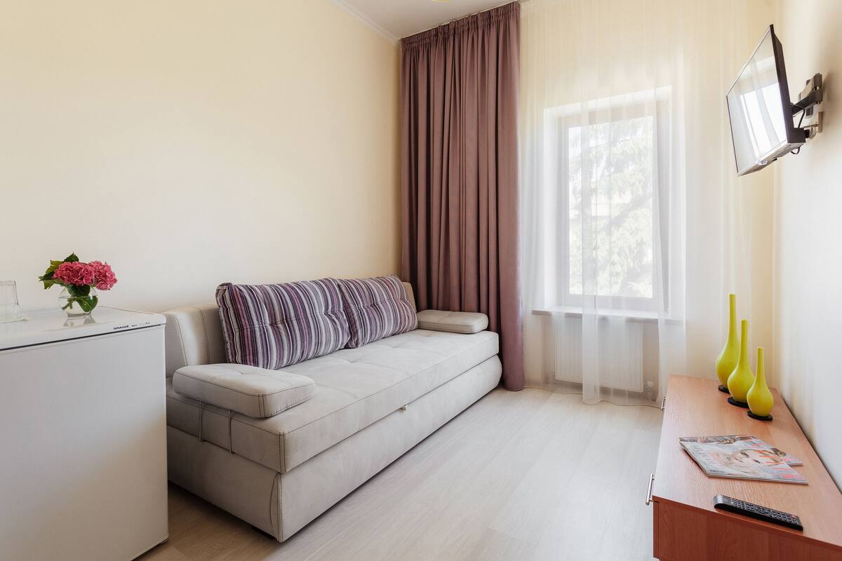 A modern living room with a sofa, a small table with a remote control, and a TV mounted on the wall.