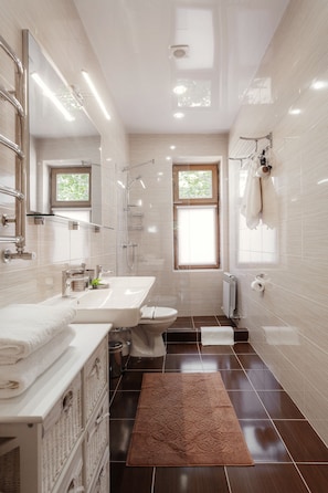 A modern bathroom with a large mirror, a bathtub, a shower, and a toilet. There is a window providing natural light and a brown rug on the floor. - Asiya Hotel (Odesa)