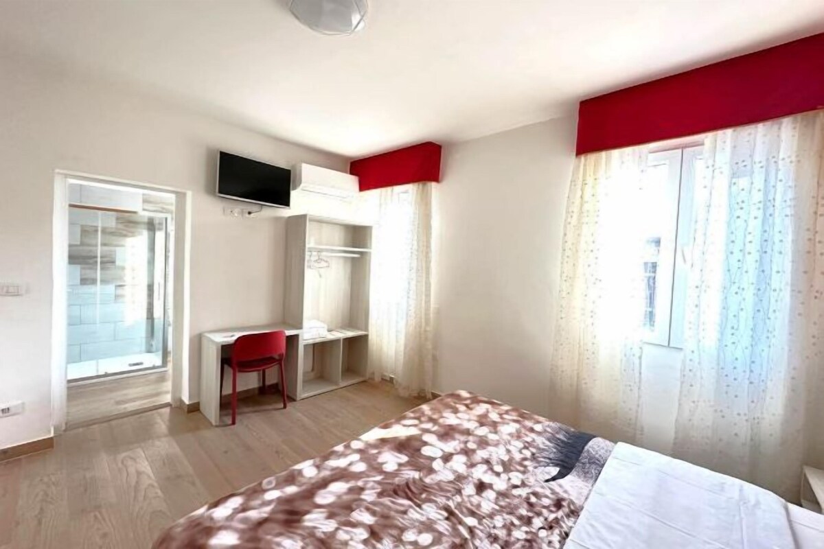 A bedroom with a bed, a desk, a chair, a TV, and a wardrobe.
