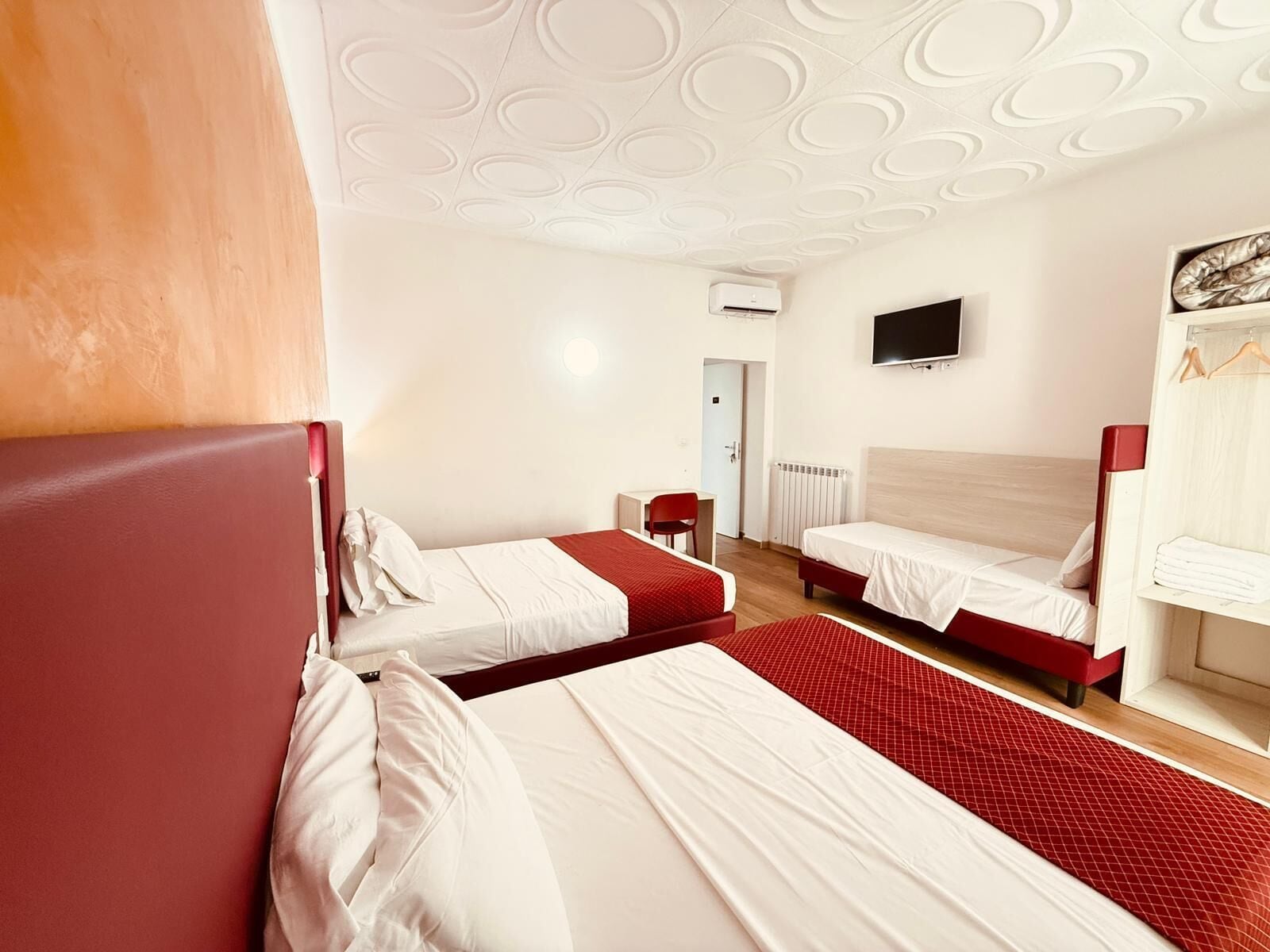Une chambre d’hôtel avec deux lits, une télévision, une armoire et une moquette rouge.