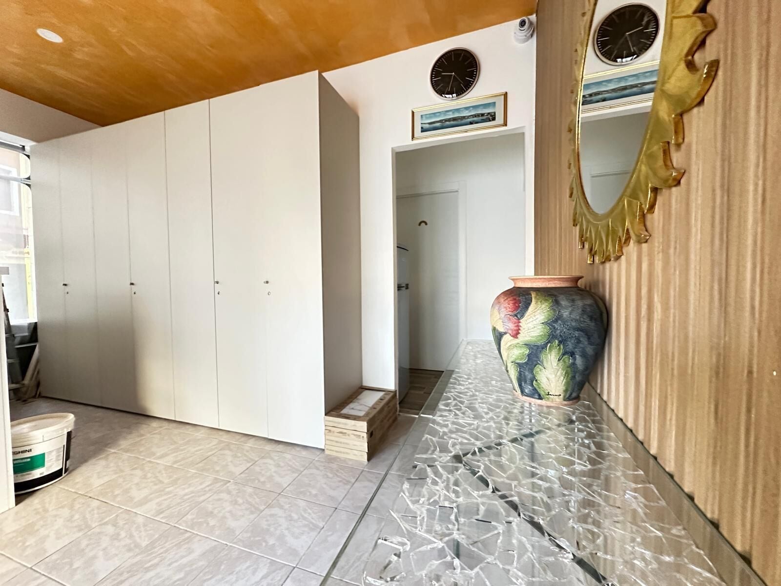 A hallway with white cabinets, a large decorative vase, and a mirror with a gold frame.