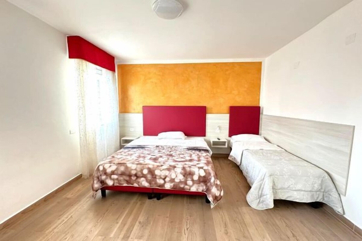 Une chambre d’hôtel avec un plancher en bois, un lit recouvert d’une couvre-lit à motifs, deux tables de chevet et un mur d’accent rouge.