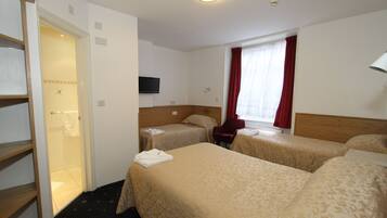 A hotel room with two single beds, a wooden headboard, a television on the wall, a window with red curtains, and a door leading to a bathroom.