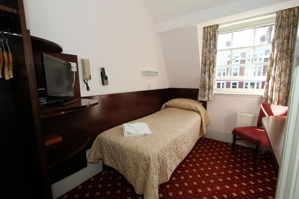 Habitación de hotel con cama, escritorio, silla, televisor y ventana con cortinas.